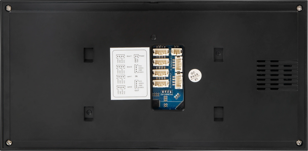 The back panel of a black electronic device, showing a central blue and white connector module, a white instruction sheet, a round silver sticker, and ventilation grilles on the right side.