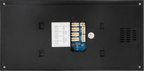 The back panel of a black electronic device, showing a central blue and white connector module, a white instruction sheet, a round silver sticker, and ventilation grilles on the right side.