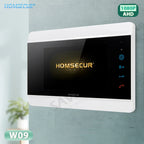 A HOMSECUR video intercom receiver with a white frame and a glossy black screen, mounted on a textured light gray wall. The screen displays the HOMSECUR logo in gold with a sparkling effect, and the right side shows blue and red icons for settings, camera, and phone.